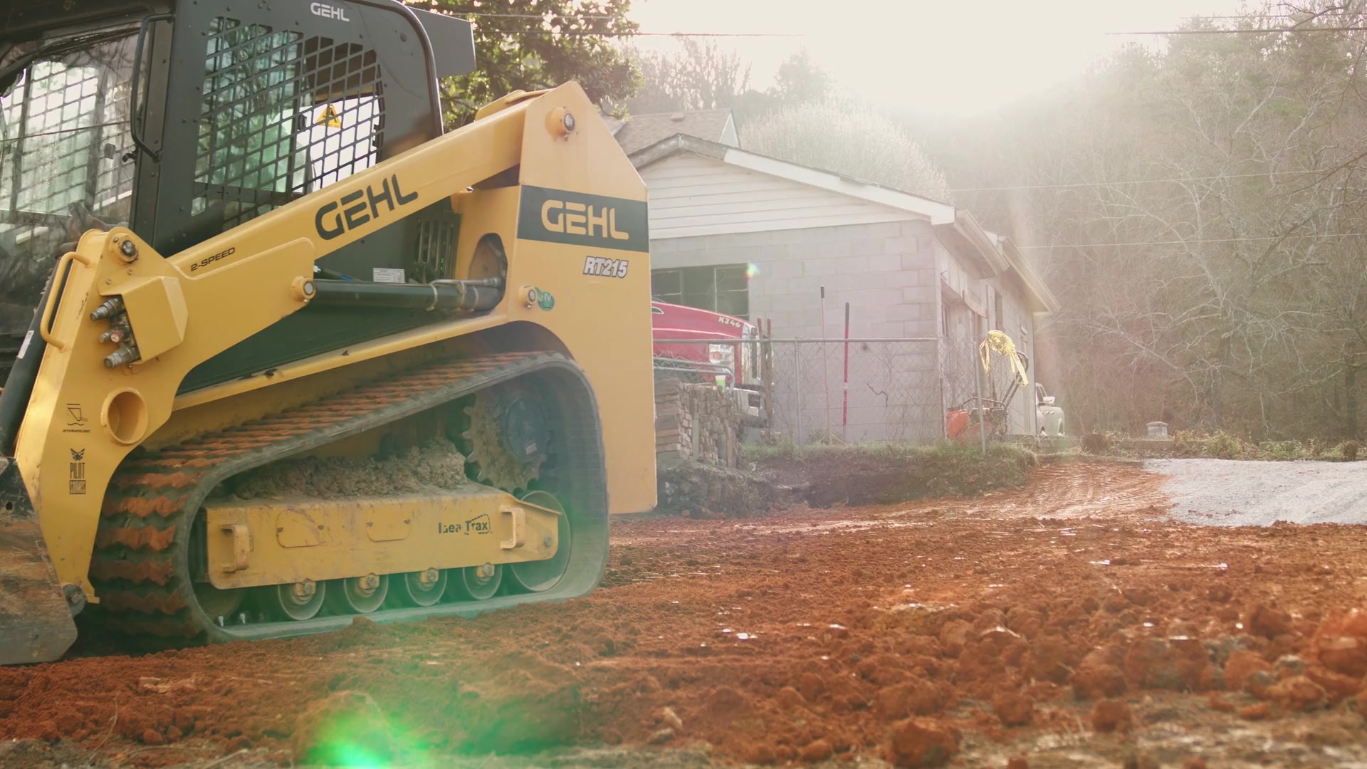 Operator using a compact tracked loader to grade red clay in a fenced residential backyard